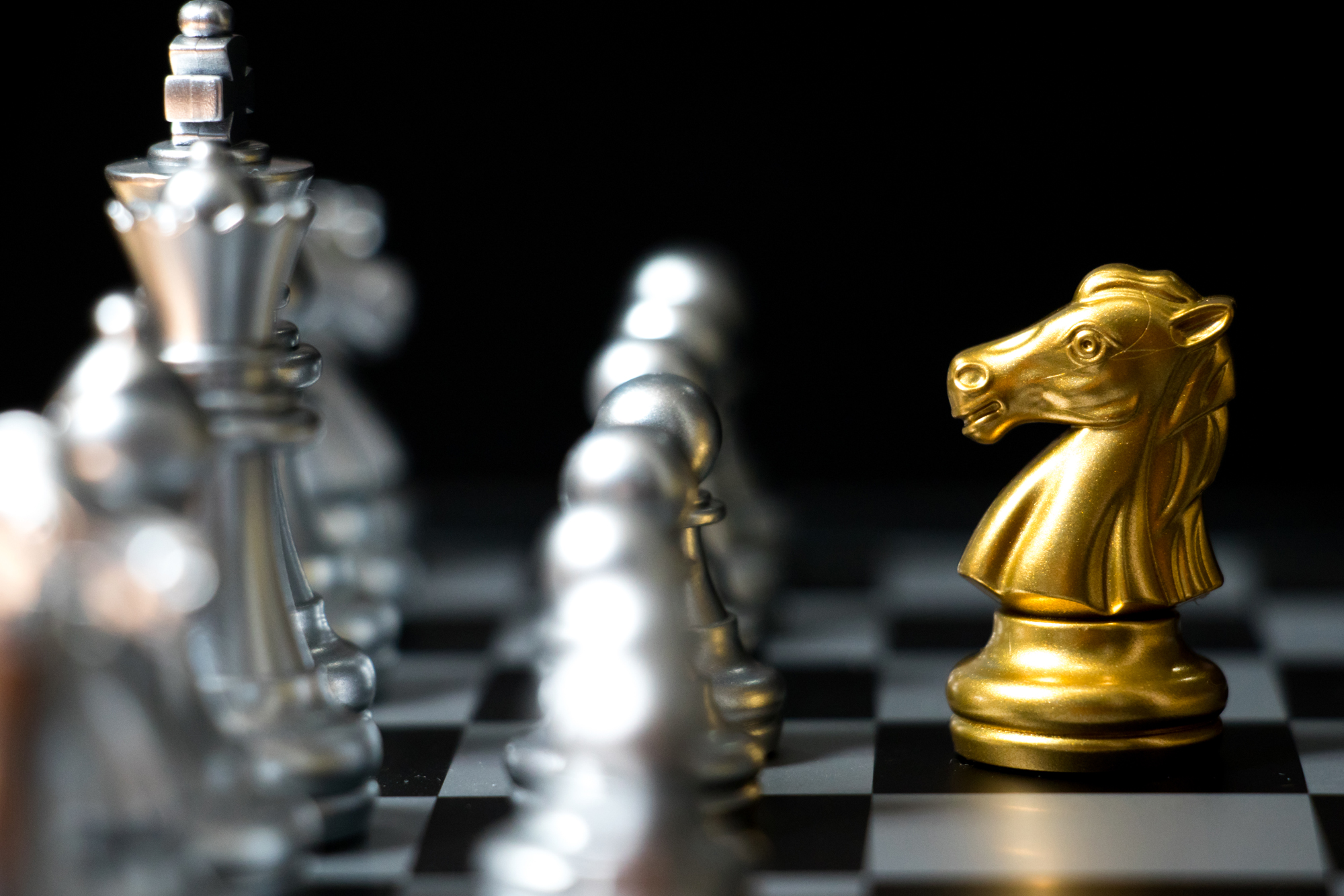 Gold horse in chess game face with the another silver team on black background (Concept for company strategy, business victory or decision)